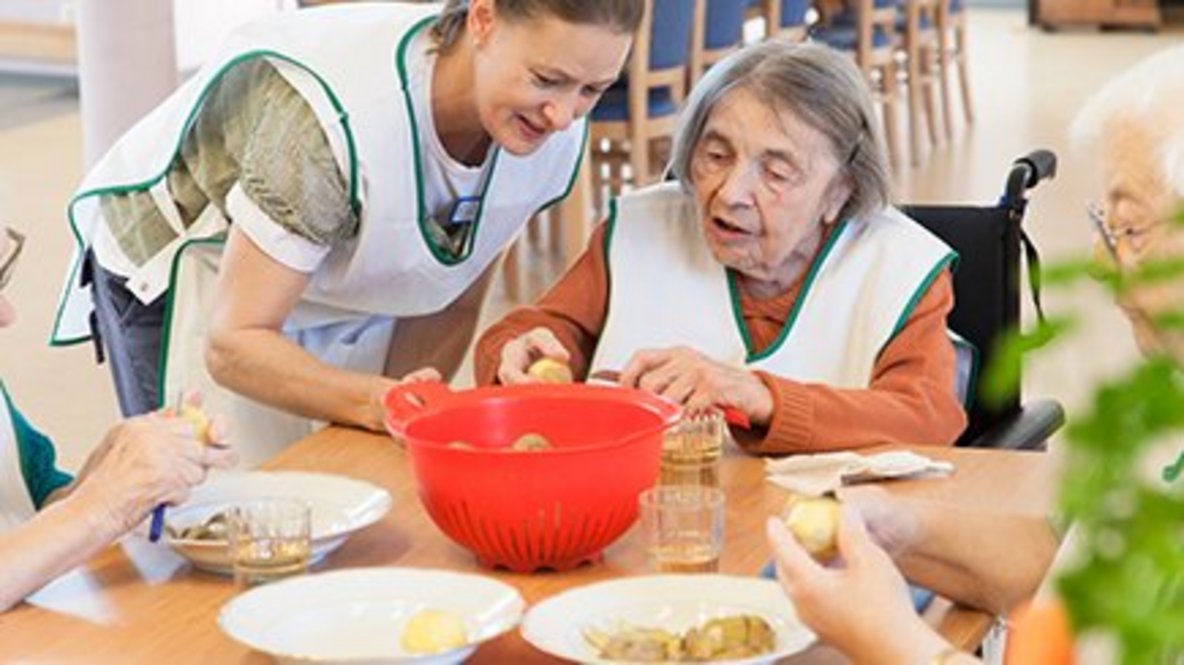 Eine Pflegekraft und eine ältere Frau bereiten gemeinsam Kartoffeln zu.