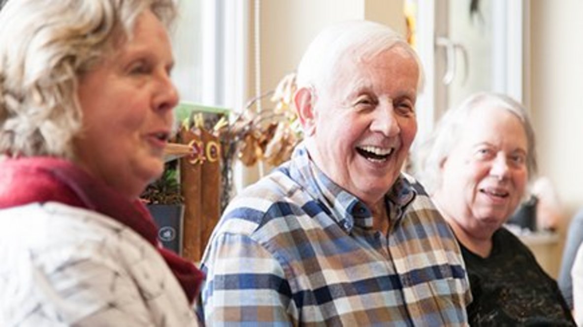 Besucher*innen und Mitarbeiterin lachen bei einer Gruppenübung